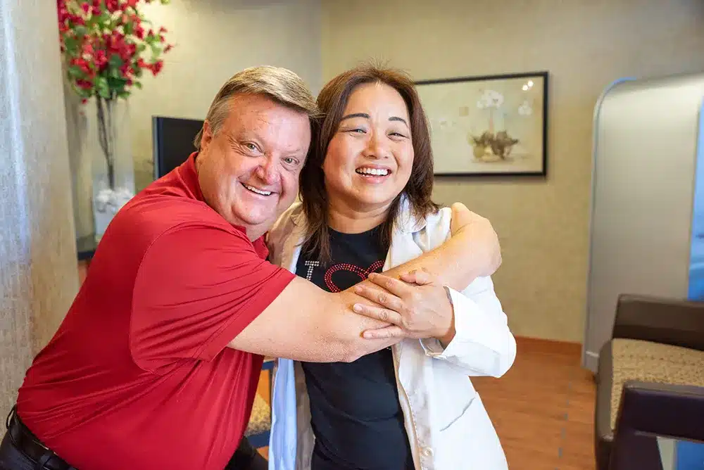 Happy patient hugging Dr. Hopkins, our Prosthodontist and dentist in Plano.